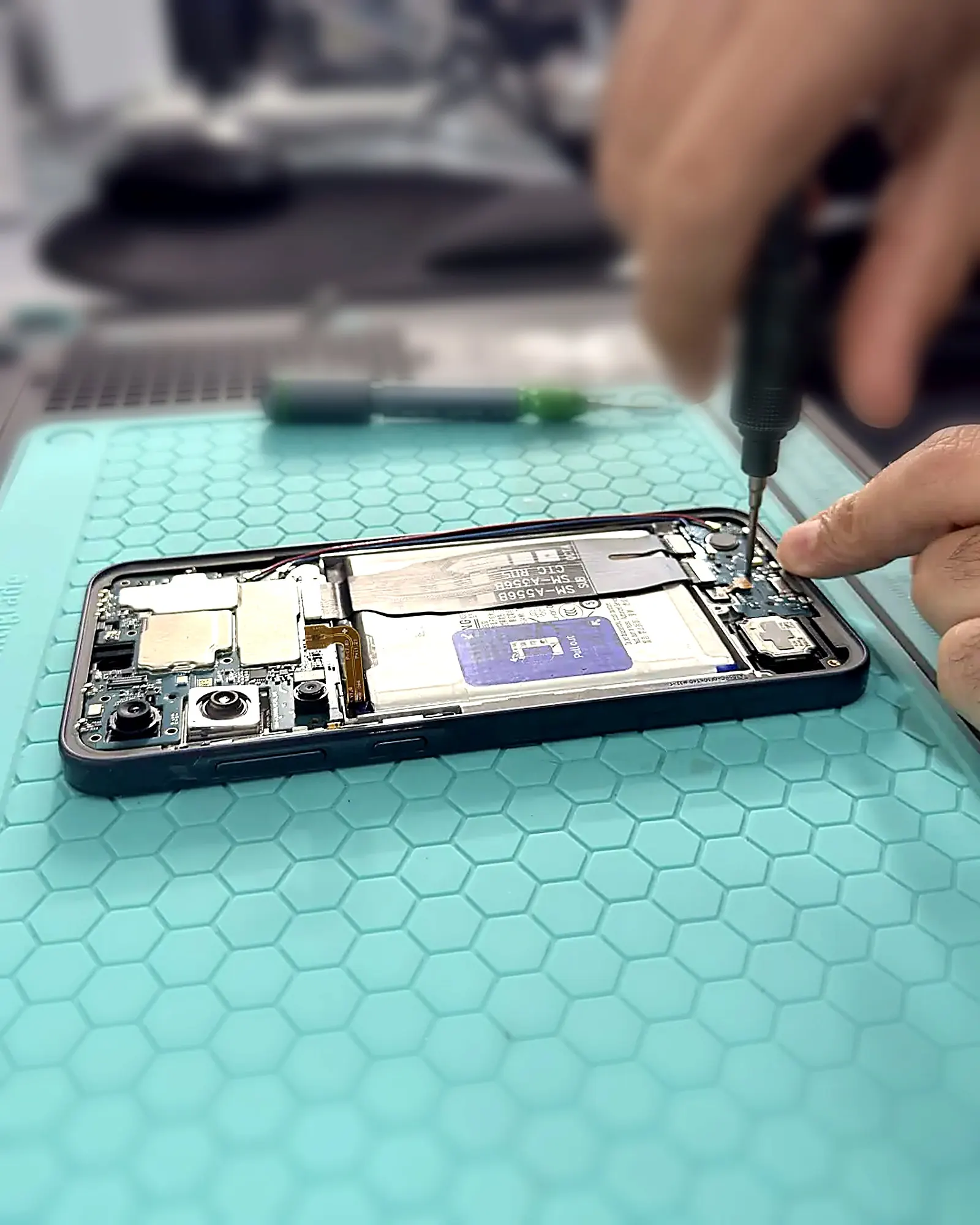 Handen met schroevendraaier die een smartphone herstellen op de werkbank van Mobile Care